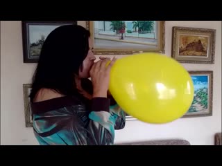 woman blows to pop a yellow balloon in her living room